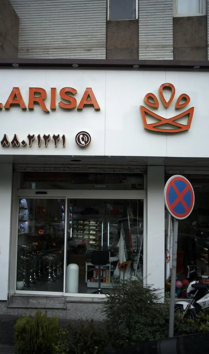 نمای خارجی فروشگاه شیرینی لاریسا: تابلوی برجسته با نام LARISA، لوگوی نارنجی، شماره تماس ۸۸۰۲۱۲۲۱ و ورودی شیشه‌ای مغازه