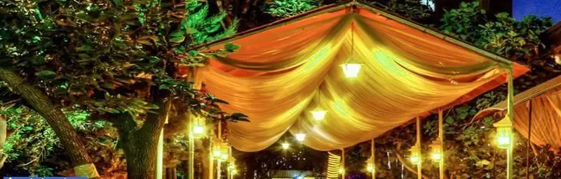 رستوران ایرانی نگارستان، فضای باز زیبا و دلنشین در شب با سقف پارچه ای نورانی و فانوس های آویز برای تجربه ای خاص و رویایی.