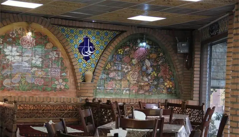 فضای دلنشین و سنتی رستوران ایرانی ساینا با دکوراسیون چشم‌نواز شامل کاشی‌کاری‌های رنگارنگ گل و بوته، طاق‌های آجری و خطاطی "علی". میز و صندلی‌های چوبی زیبا آماده پذیرایی از میهمانان.