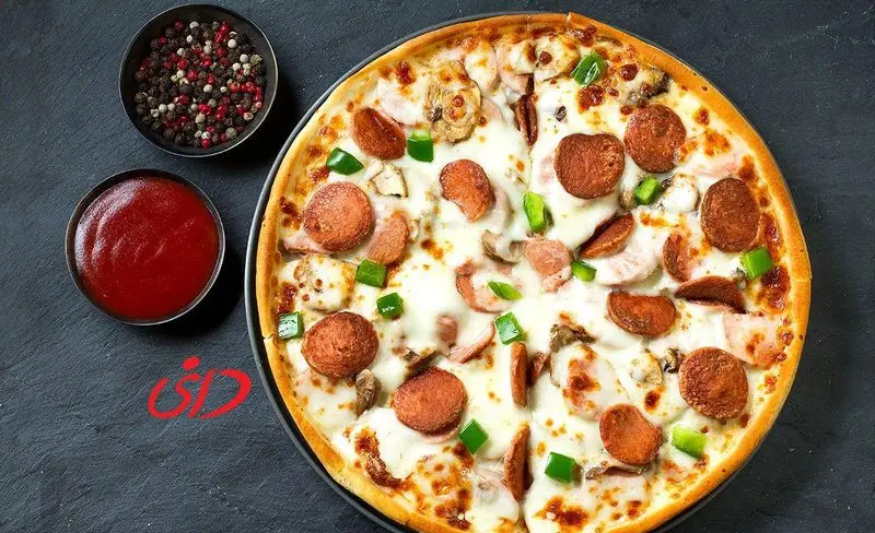 عکس پیتزا پپرونی و قارچ دانی با فلفل دلمه ای روی میز مشکی به همراه سس کچاپ و فلفل های رنگی. سفارش آنلاین پیتزا دانی.