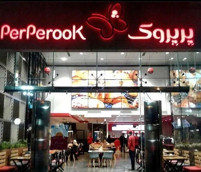 تصویری از نمای شبانه شعبه فست فود پرپروک با نورپردازی قرمز جذاب بر روی نام تجاری و محیط داخلی گرم و دعوت کننده.