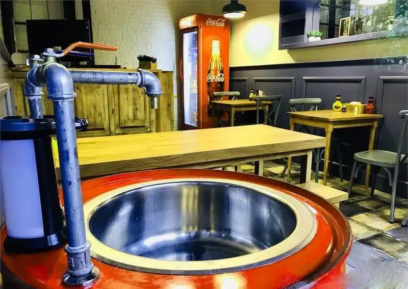 فضای داخلی جذاب و مدرن برگر اریک برگر با میزهای چوبی، دیوارهای تیره، شیر آب صنعتی و یخچال کوکا کولا، محیطی دلنشین برای صرف برگر ارائه می‌دهد.