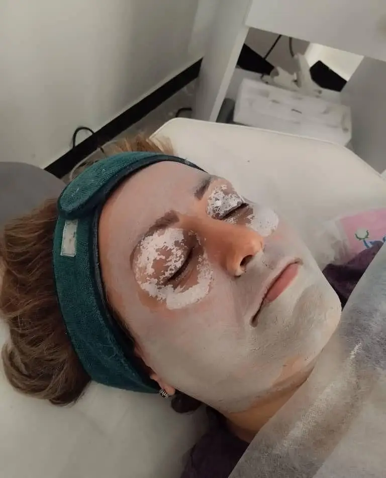 مراحل فیشیال و پاکسازی تخصصی پوست صورت زن در کلینیک زیبایی با ماسک خاک رس و پدهای مخصوص دور چشم برای جوانسازی پوست