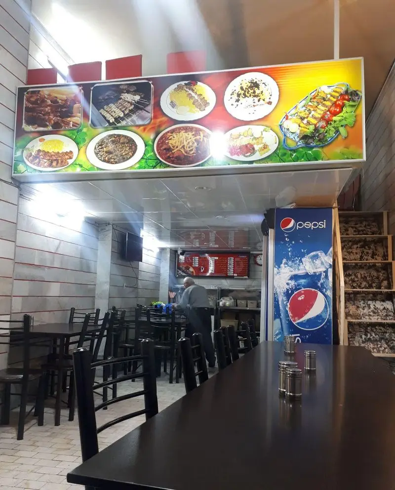 فضای داخلی رستوران امامی با میز و صندلی‌های مرتب و تمیز، تابلوی منوی بزرگ غذاهای لذیذ ایرانی شامل کباب و برنج.