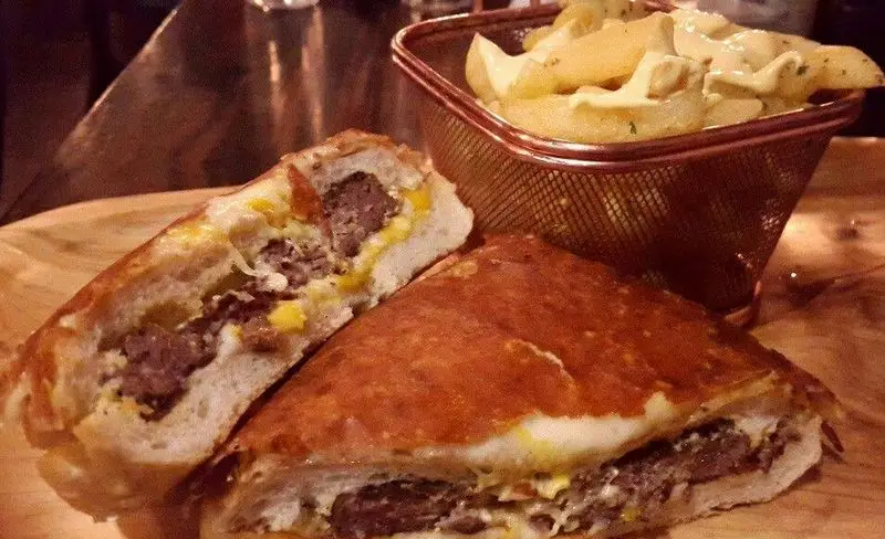 ساندویچ برگر بزرگ میخوش با پنیر آب شده و سیب زمینی های ضخیم سرخ شده با سس مخصوص، یک غذای پرطرفدار و خوشمزه در رستوران می خوش.