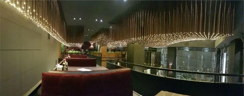 فضای داخلی رستوران میخوش با طراحی مدرن و نورپردازی چشمگیر سقفی، شامل چراغ‌های آویز و ردیف‌های چوبی بلند، محیطی دلنشین برای تجربه غذا.