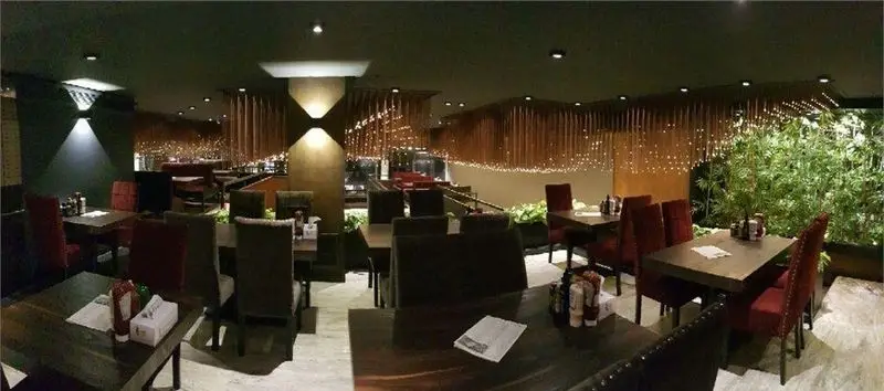 فضای داخلی شیک و دنج رستوران میخوش با دکوراسیون چوبی، نورپردازی گرم و ریسه‌ای، میز و صندلی‌های راحت، مناسب برای تجربه غذایی دلپذیر.