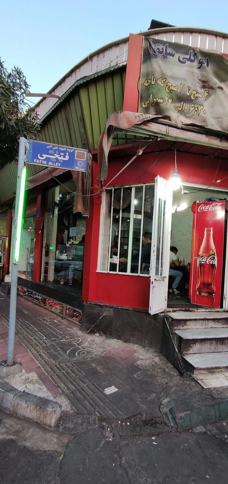 نمای خارجی طباخی توکلی، رستوران کله پاچه محبوب، واقع در کوچه شهید علی اکبر فتحی. تابلوی خیابان و ورودی قرمز فروشگاه دیده می‌شود.