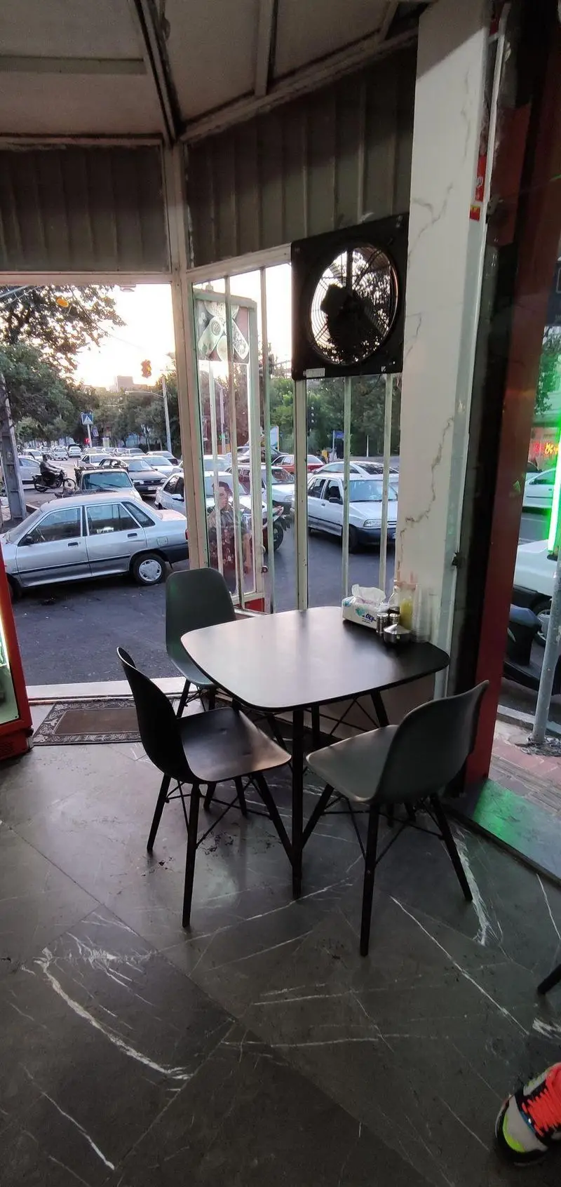 فضای داخلی دنج و دلنشین طباخی توکلی، با میز و صندلی‌های مدرن و شیک، مشرف به چشم‌انداز خیابان و ترافیک عصرگاهی.