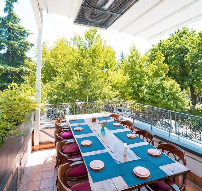 رستوران مس توران: فضای باز و سرسبز با میز ناهارخوری چوبی بزرگ، آماده پذیرایی از مهمانان در تراس مشرف به طبیعت زیبا.