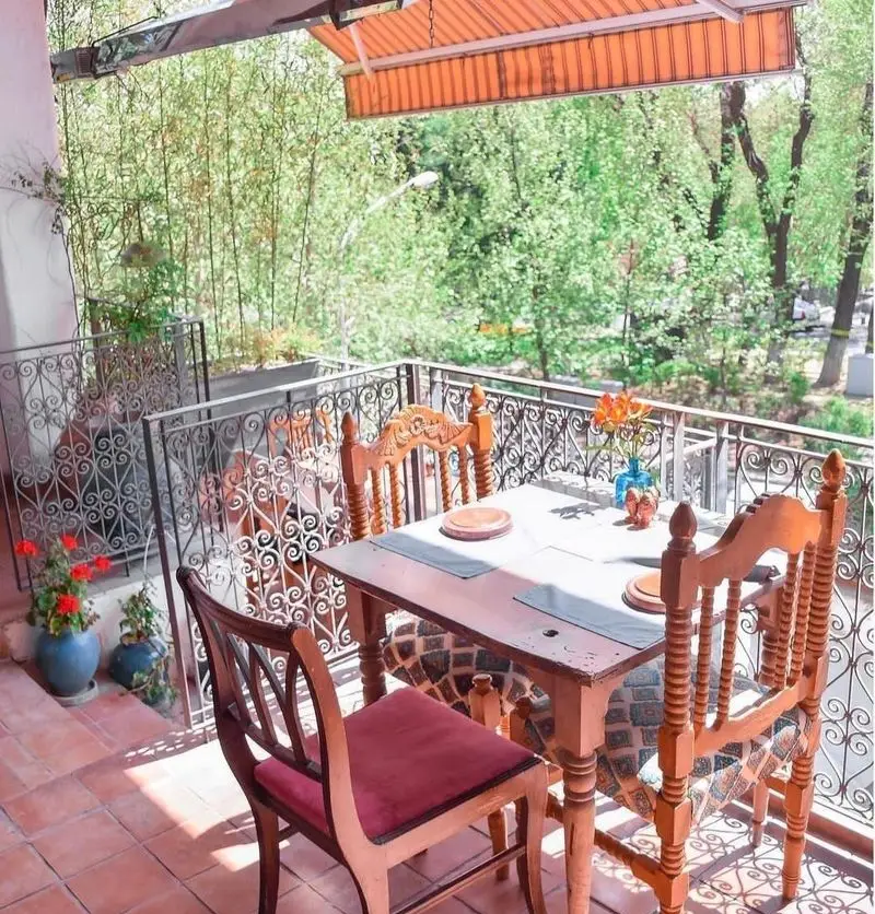 بالکن زیبای رستوران مس توران با سایبان نارنجی، نرده‌های فرفورژه و میز ناهارخوری چوبی در فضایی سرسبز و دلنشین.
