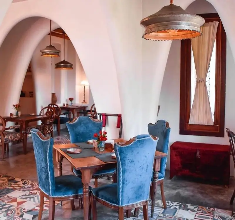 تصویر داخلی رستوران مس توران: فضایی شیک با طاق‌های زیبا، صندلی‌های مخمل آبی، میزهای چوبی، لوسترهای مسی و کفپوش سنتی.