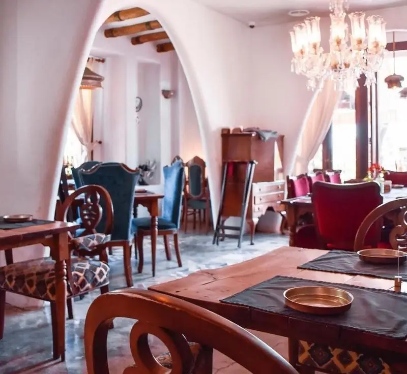 دکوراسیون داخلی رستوران مس توران با فضای سنتی و دلنشین، میز و صندلی‌های چوبی شیک، لوستر کریستالی، و دیوارهای قوسی سفید.