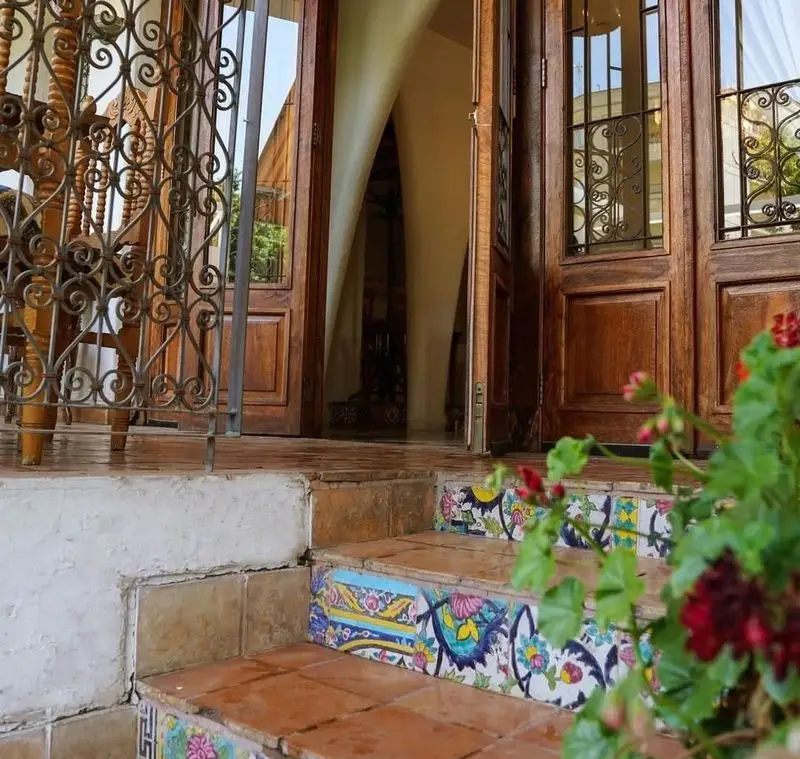 ورودی جذاب رستوران مس توران با درهای چوبی، پله‌های کاشی‌کاری سنتی رنگارنگ و نرده فلزی زیبای طرح‌دار.