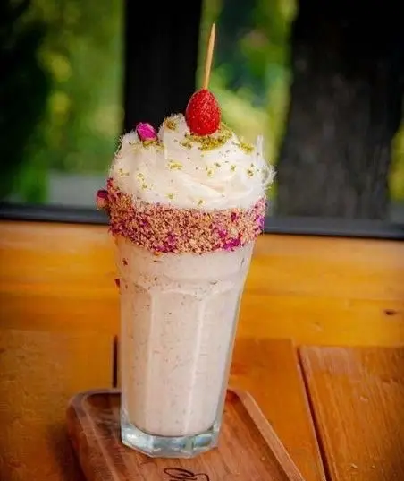 میلک شیک خوشمزه با خامه، مغز پسته و تمشک تازه، تزئین شده با گلبرگ خشک گل محمدی در رستوران ایتالیایی شله.