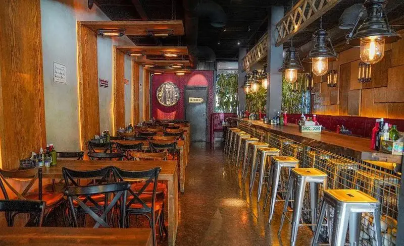 فضای داخلی فست فود میخوش با دکوراسیون صنعتی و گرم، شامل میز و صندلی‌های چوبی، کانتر بار، صندلی‌های فلزی و نورپردازی خاص. محیطی دلنشین برای صرف فست فود.