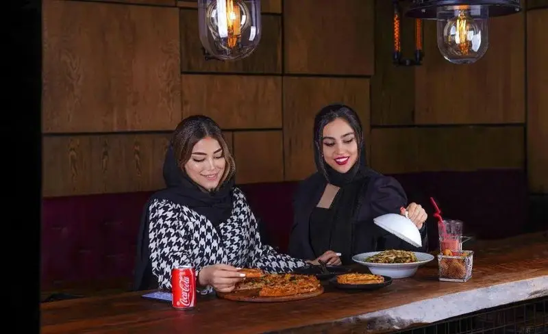 دو خانم شاد در رستوران فست فود میخوش در حال لذت بردن از پیتزا، پاستا و نوشیدنی، تجربه‌ای دلنشین با دوستان.