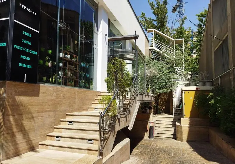 تصویر نمای بیرونی رستوران فست فود میخوش با ورودی پله‌ای، شیشه‌های بزرگ، تابلوی منوی پیتزا، پاستا، مرغ سوخاری، استیک و برگر در طراحی مدرن.