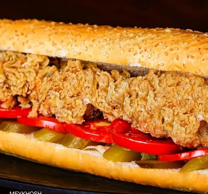 ساندویچ مرغ سوخاری مجلسی و بزرگ فست فود میخوش، با نان کنجدی طلایی، گوجه فرنگی تازه و خیارشورهای ترد.