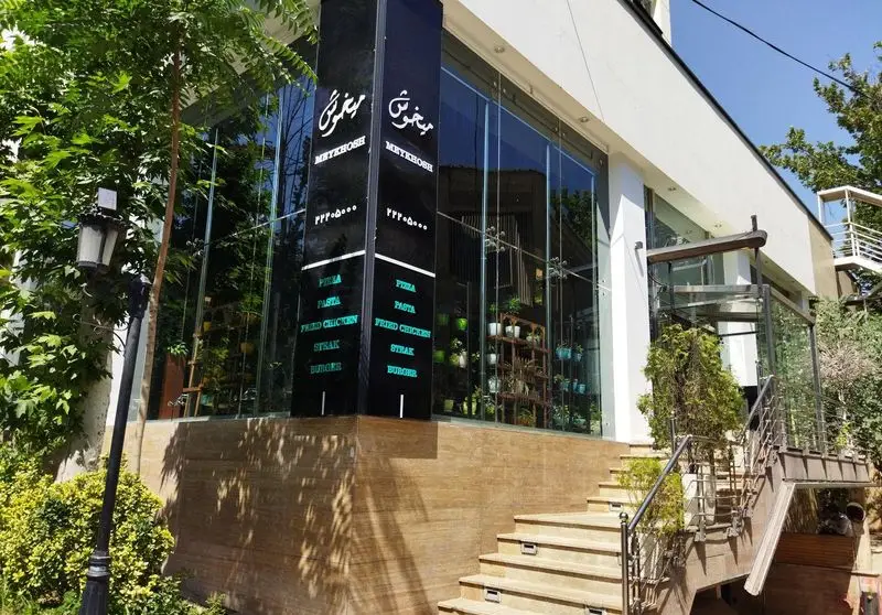 فست فود میخوش، رستورانی مدرن و جذاب با نمای شیشه‌ای، پله‌های ورودی، فضای سبز و منوی متنوع شامل پیتزا، پاستا، مرغ سوخاری و برگر.