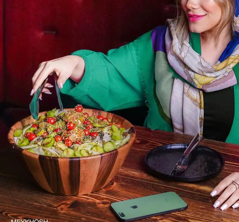 خانمی در فست فود میخوش در حال سرو سالاد تازه و سرشار از گوجه گیلاسی و سبزیجات، نمادی از غذای سالم و تجربه دلنشین.