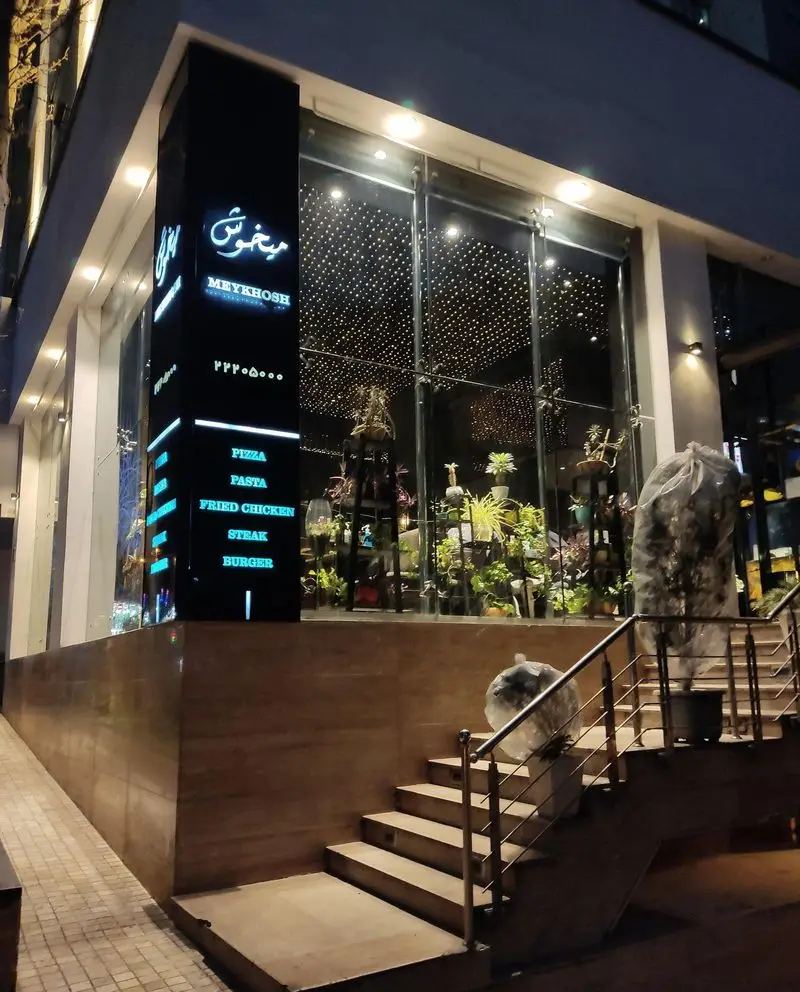 نمای بیرونی شبانه فست فود و رستوران میخوش با تابلوی درخشان. ارائه منوی متنوع پیتزا، پاستا، مرغ سوخاری، استیک و برگر.