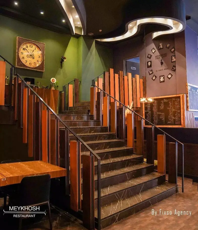 دکوراسیون داخلی شیک و مدرن فست فود میخوش با پله‌های مرمری، نرده‌های چوبی و فلزی، و نورپردازی جذاب. محیطی دلنشین برای مشتریان.