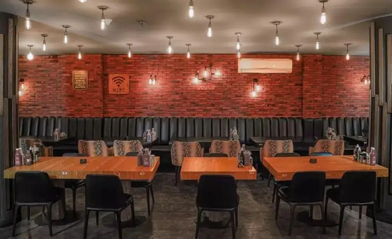 فضای داخلی دنج و مدرن فست فود میخوش با دیوارهای آجری، میزهای چوبی روشن و صندلی‌های مشکی، نورپردازی صنعتی و دکور جذاب.