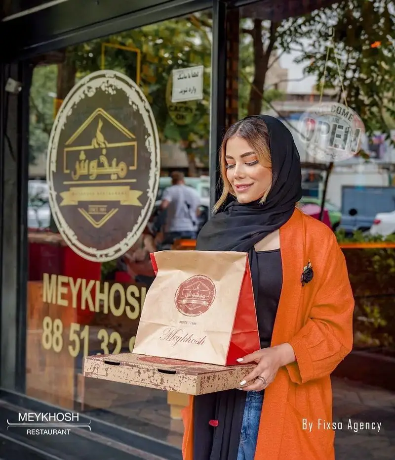 بانویی در حال تحویل سفارش پیتزا و غذای آماده از فست فود میخوش، نشان‌دهنده سرویس بیرون‌بر و سفارش آنلاین درب منزل از رستوران Meykhosh.