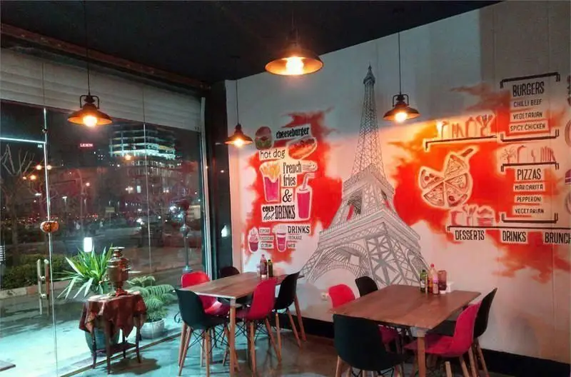 نمای داخلی جذاب فست فود پرگوک در شب با دکوراسیون مدرن، میز و صندلی، دیوارنگاره برج ایفل و منوی متنوع برگر و پیتزا.