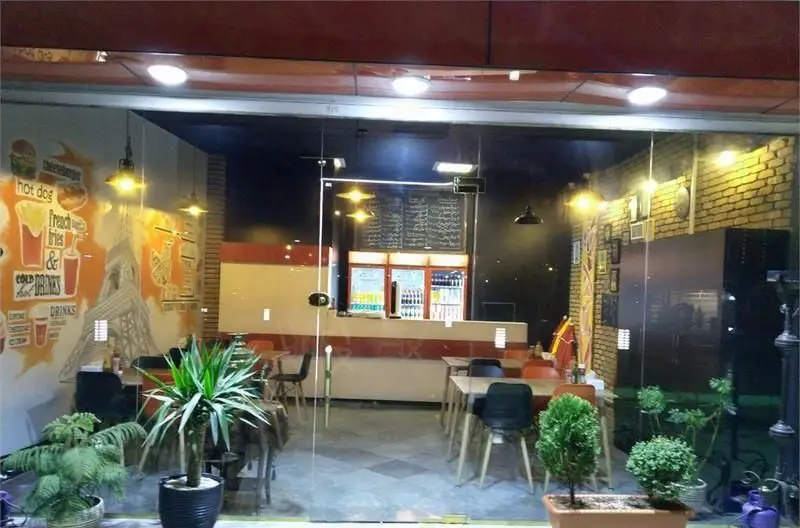 فست فود پرگوک: نمایی از فضای داخلی دلنشین با میز و صندلی، پیشخوان سفارش، منوی غذا و نوشیدنی به همراه تزئینات هات داگ و ایفل.