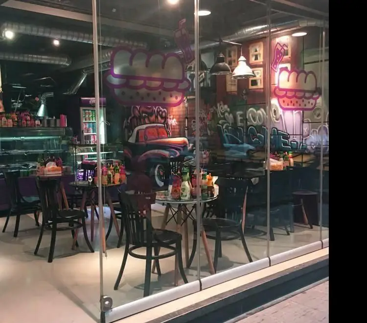 فضای داخلی کافه فست فود شکلات پلاس با طراحی مدرن و نقاشی‌های دیواری گرافیکی، شامل میز و صندلی و ویترین غذا. محیطی جذاب و رنگارنگ برای مشتریان.