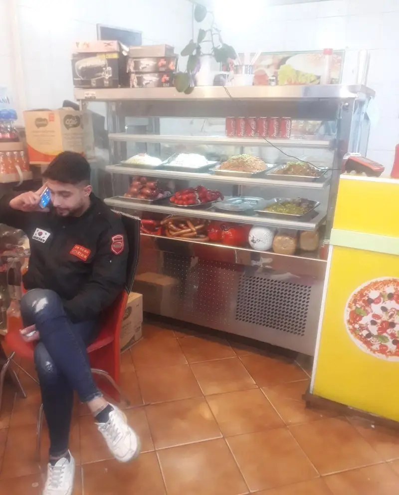 فضای داخلی دلنشین ساندویچ Ben ۱۰، شامل مشتری در حال مکالمه و ویترین غذاهای متنوع و خوشمزه فست فود.