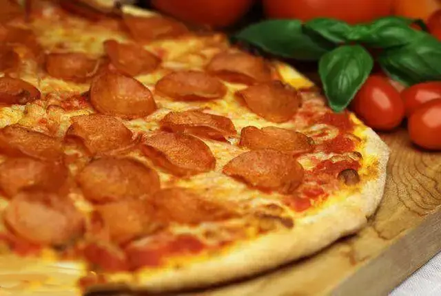 تصویر نزدیک از پیتزا پپرونی خوشمزه و داغ پیتزا هات اندرزگو، با پنیر کش‌دار و برش‌های گوشت لذیذ، روی میز چوبی آماده سرو.