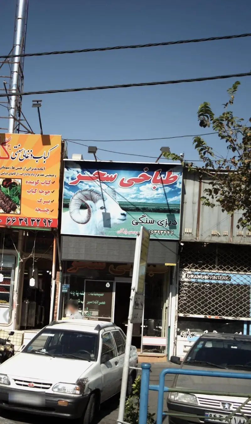 نمای بیرونی طباخی سحر با تابلویی روشن از گوسفند شاخدار و آسمان آبی، ارائه دهنده دیزی سنگی و کله پاچه در تهران.