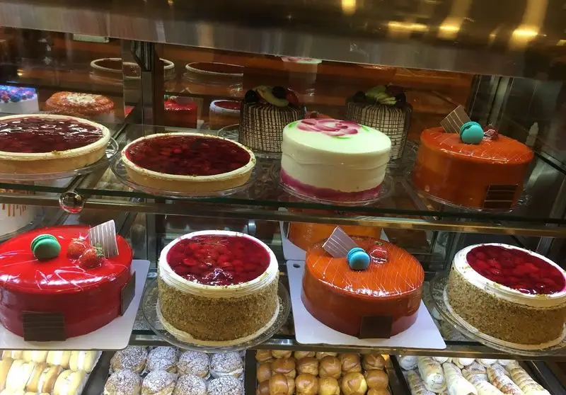 ویترین جذاب شیرینی سالوت تهرانپارس شامل کیک‌های تولد متنوع، تارت‌های میوه‌ای رنگارنگ و شیرینی‌های تازه و باکیفیت.