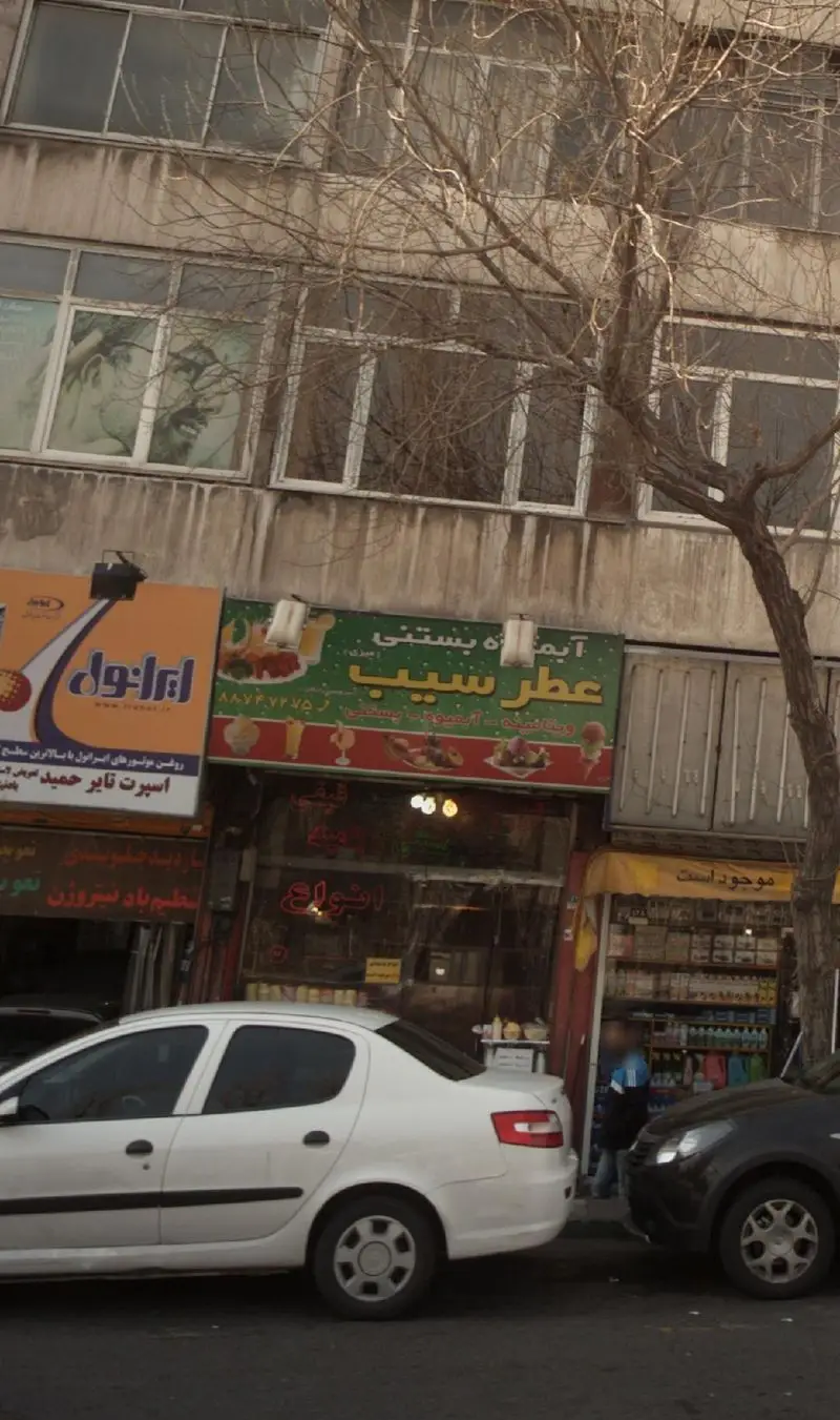 تابلوی آبمیوه بستنی عطر سیب در خیابان ایران. این مغازه انواع آبمیوه و بستنی را ارائه می‌دهد و در کنار آن خودروها پارک شده‌اند.