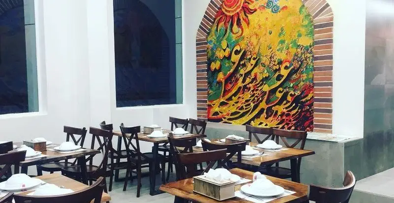 فضای داخلی رستوران آقای دیزی با میز و صندلی‌های چوبی، دکوراسیون سنتی و نقاشی دیواری رنگارنگ، مکانی دلنشین برای سرو دیزی و غذای ایرانی.