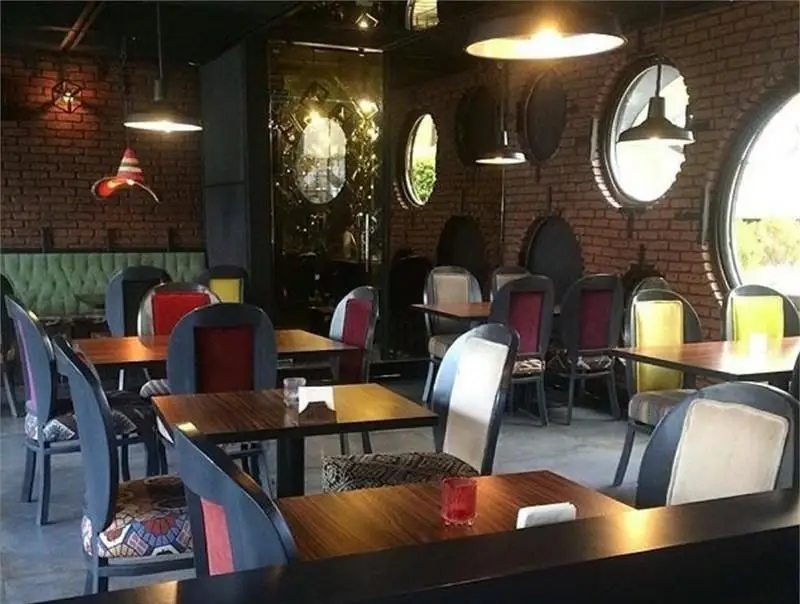 فضای داخلی دنج و مدرن کافی شاپ جیلیز با دیوارهای آجری، پنجره‌های گرد و مبلمان رنگارنگ برای تجربه یک دورهمی دلنشین.