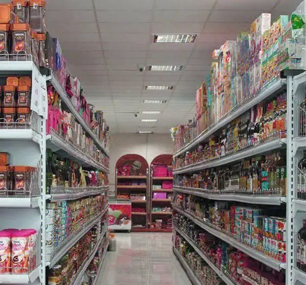 قفسه‌های بلند و چیدمان منظم محصولات متنوع در راهروی فروشگاه کافی شاپ جیلیز، شامل انواع قهوه، نوشیدنی‌ها و مواد غذایی آماده خرید مشتریان