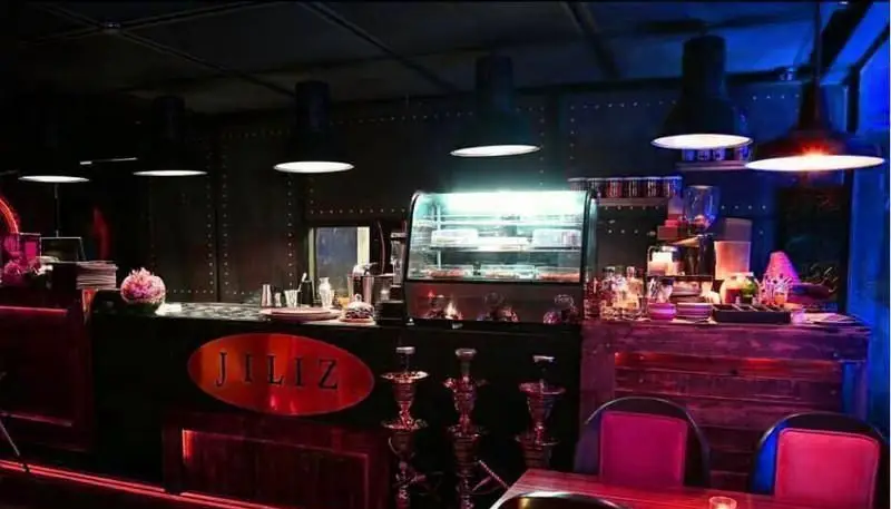 فضای داخلی شیک و مدرن کافی شاپ جیلیز با پیشخوان، نورپردازی خاص قرمز و آبی، نمایشگر دسر و قلیان‌های زیبا.