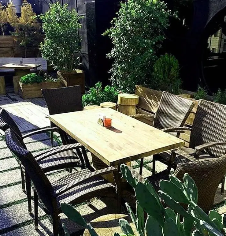 فضای باز دلنشین کافی شاپ جیلیز، با میزهای چوبی و صندلی‌های حصیری شیک، محیطی آرام برای استراحت و لذت بردن از قهوه و نوشیدنی در فضایی سبز.