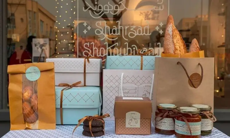 بسته‌بندی‌های شیک و جذاب محصولات کافه شیرینی فم‌ شیک شامل نان تازه، کوکی شکلاتی، شیشه‌های مربا و جعبه‌های هدیه زیبا.