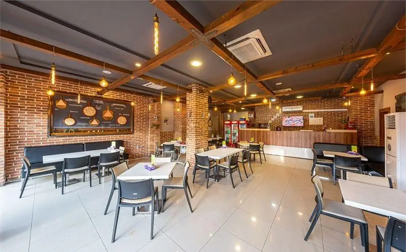 پیتزا سیب ۳۶۰: نمای داخلی یک پیتزا فروشی مدرن با دیوارهای آجری، دکوراسیون چوبی سقف، میز و صندلی‌های راحت و نورپردازی صنعتی زیبا.