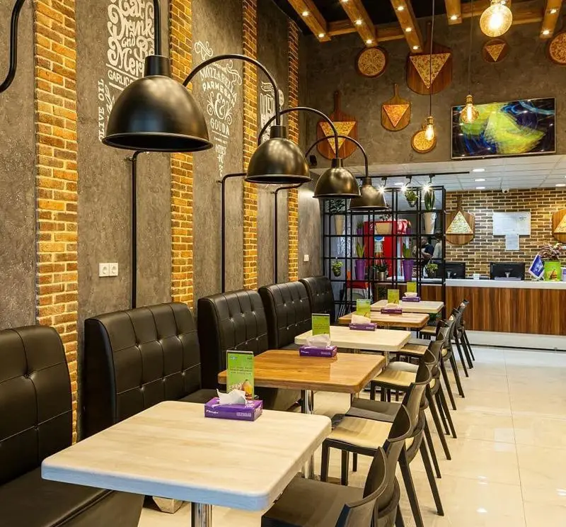 فضای داخلی مدرن و دنج پیتزا سیب ۳۶۰ با دیوارهای آجری، مبلمان راحت و نورپردازی خاص برای لذت بردن از پیتزا.