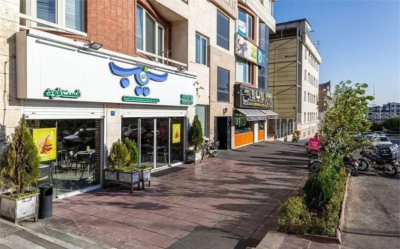 نمای خارجی رستوران فست فود پیتزا سیب ۳۶۰ با تابلوی آبی، شیشه‌های بزرگ و گلدان‌های سبز، فضایی دلنشین در کنار پیاده‌رو.