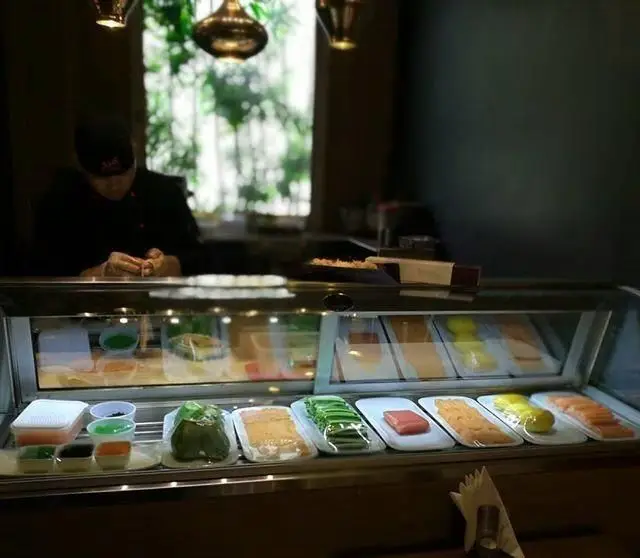 سرآشپز کنزو اکسپرس در رستوران ژاپنی مشغول آماده‌سازی سوشی‌های تازه. ویترین شیشه‌ای پر از مواد اولیه درجه یک برای سوشی و رول‌های آماده.