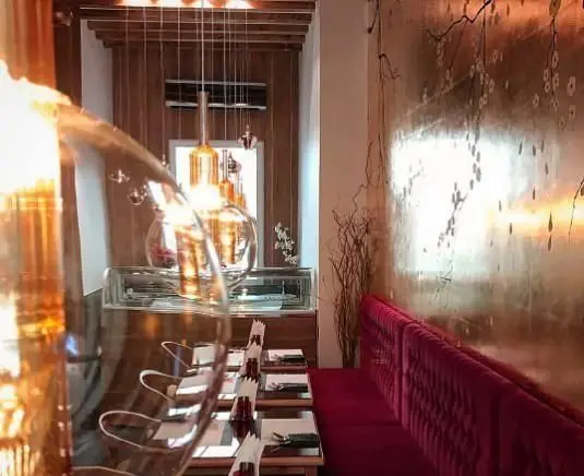 فضای داخلی شیک و مدرن رستوران ژاپنی کنزو اکسپرس با دکوراسیون چشم‌نواز، شامل نیمکت قرمز مخملی و دیوار طرح‌دار طلایی، آماده پذیرایی از میهمانان.