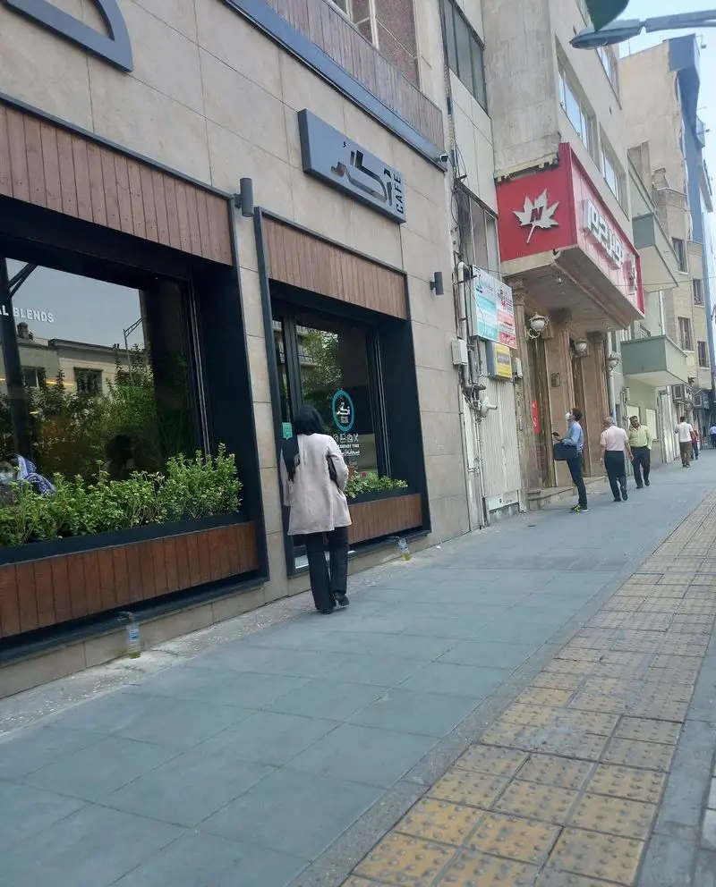 نمای جلویی کافه آگر با تابلوی روشن "کافه آگر" و "CAFE". ورودی مدرن با پنجره‌های بزرگ، گلدان‌های سبز، و رهگذران در خیابان.