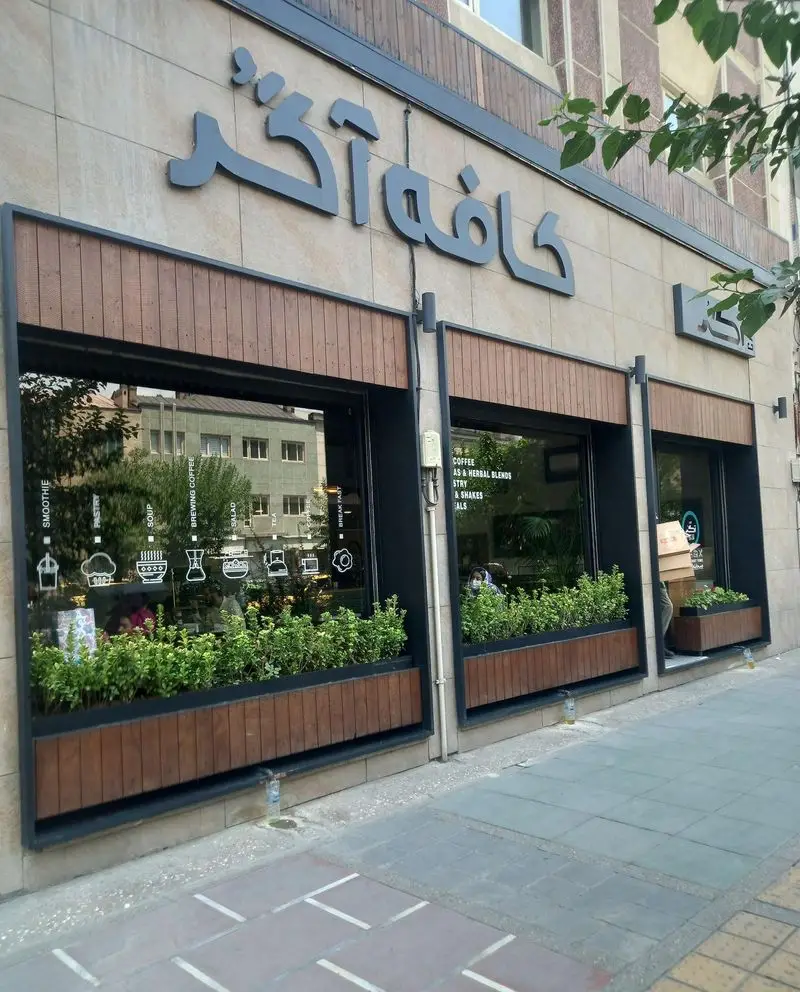 نمای ورودی کافه آگر، کافه‌ای مدرن با پنجره‌های بزرگ، گلدان‌های سرسبز و منوی صبحانه، قهوه و انواع نوشیدنی.